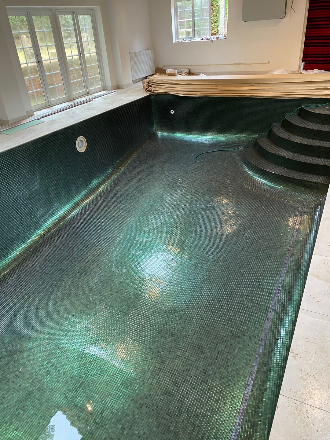 The entire pool has been retiled, with mosaic tile accents in green incorporated along the waterline, complemented by contrasting bands and borders.