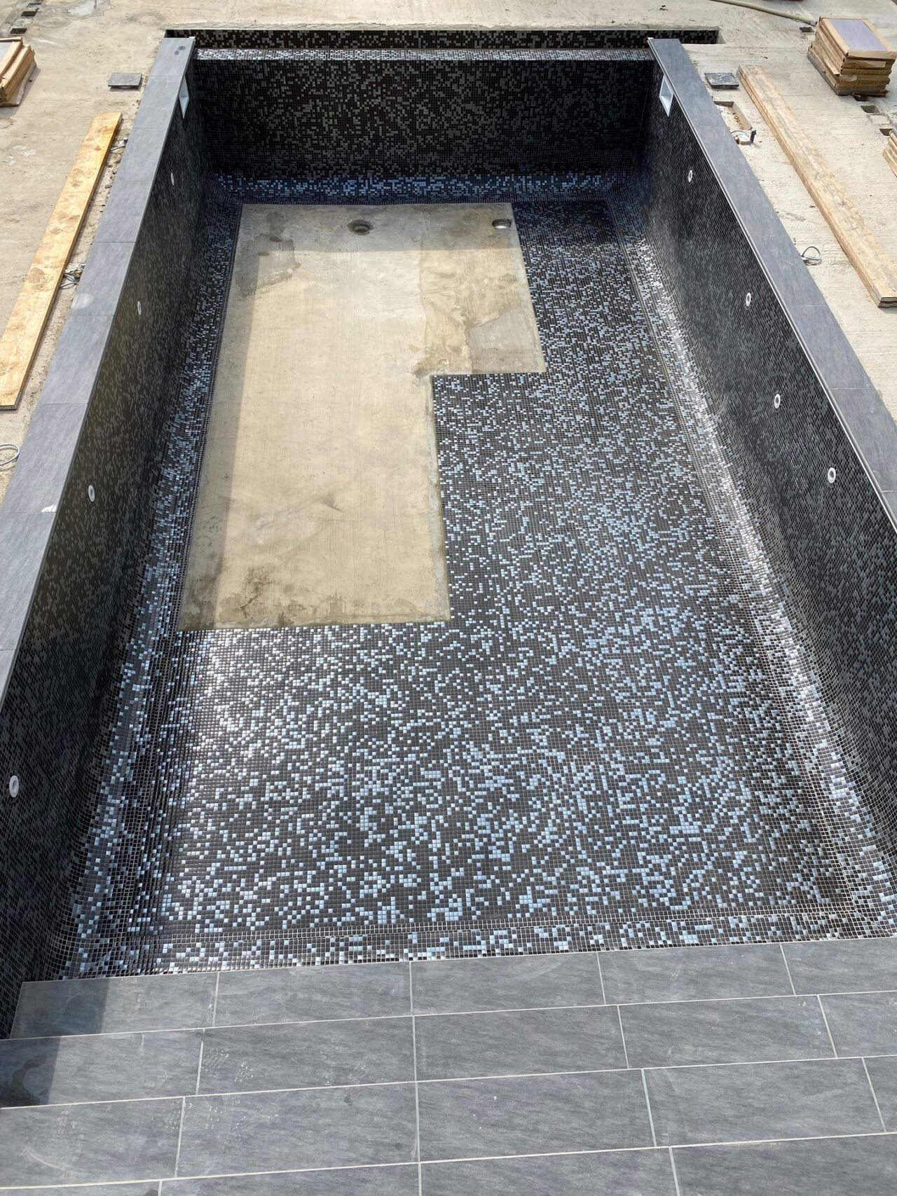 black and silver mosaic tiles being installed at the bottom of the swimming pool