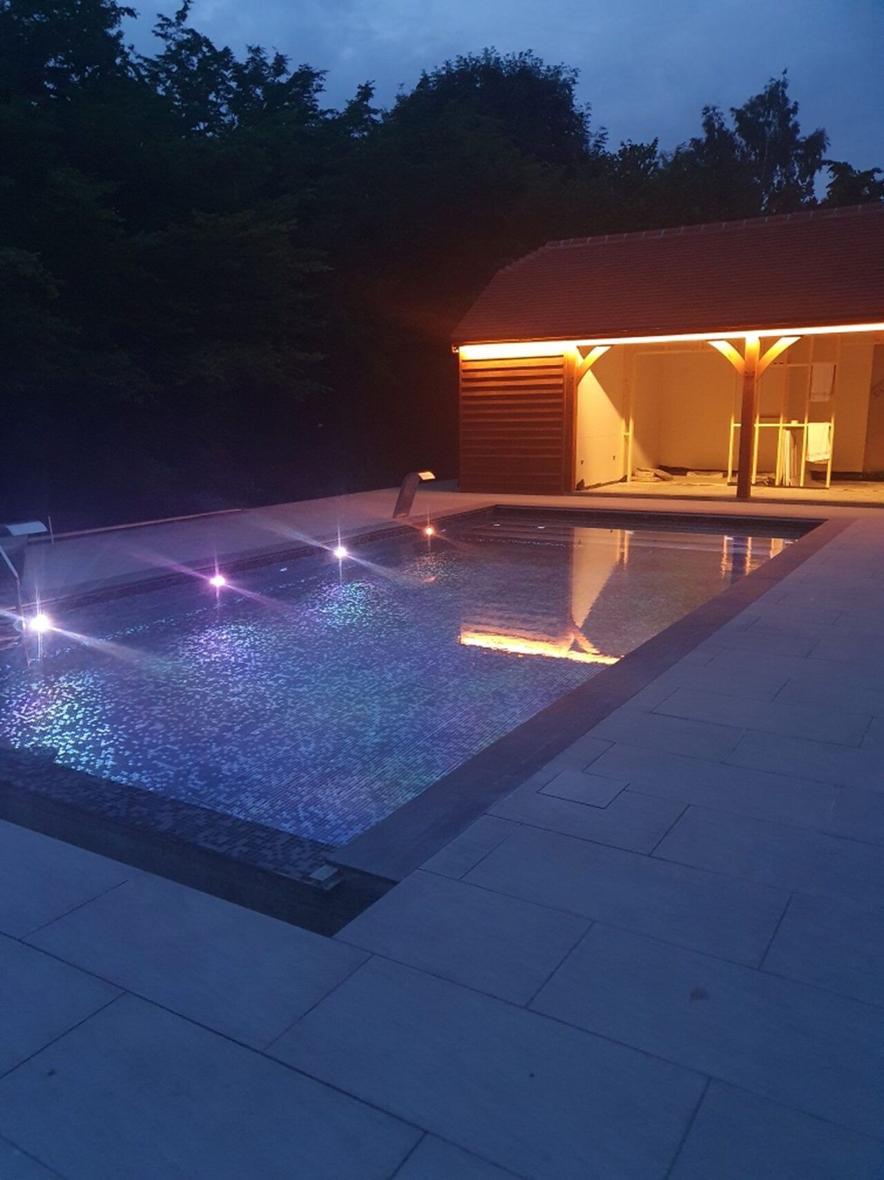 Finished evening shot of the swimming pool and pool house with lights