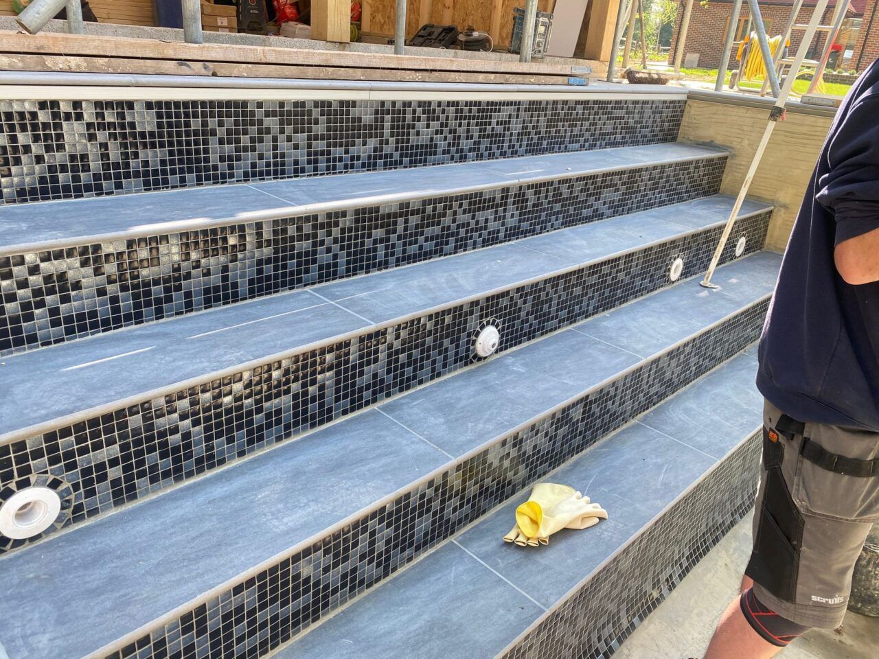 The steps also getting the same black and silver mosaic tiles like the swimming pool